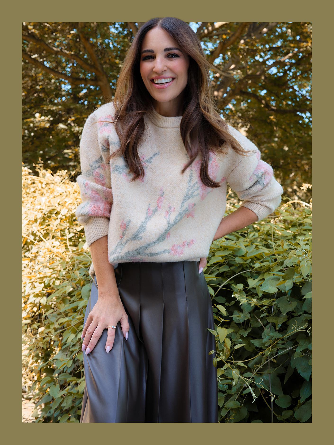 Person wearing cream jumper with pastel pink and blue pattern paired with grey wide-leg trousers outdoors.
