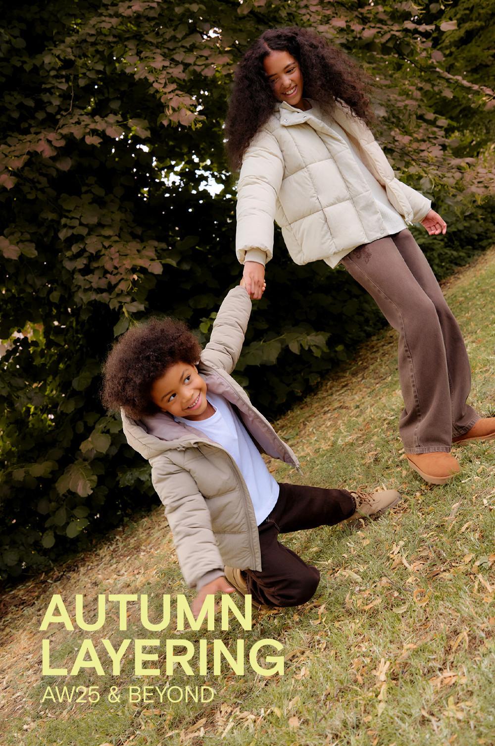 Two people wearing cream puffer jackets holding hands outdoors against a leafy background.