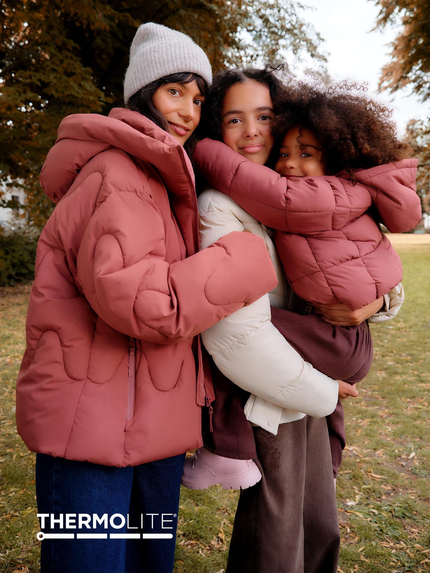 Family wearing matching dusty pink and cream puffer jackets from Thermolite outdoors in autumn setting.