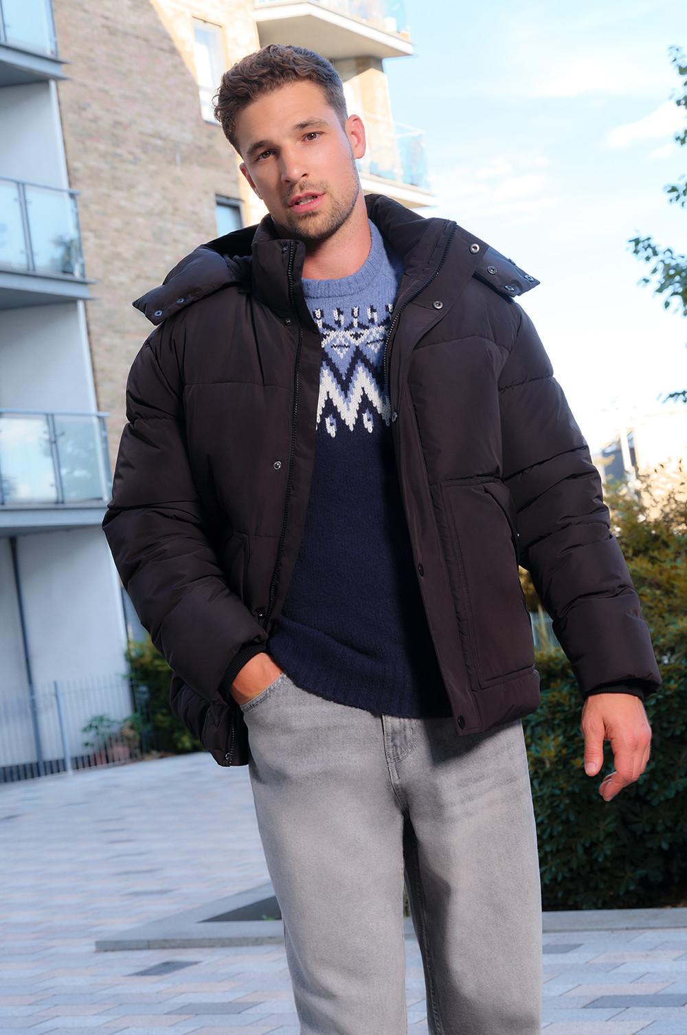 Black quilted puffer jacket worn with patterned knit sweater and light gray jeans in an urban setting.