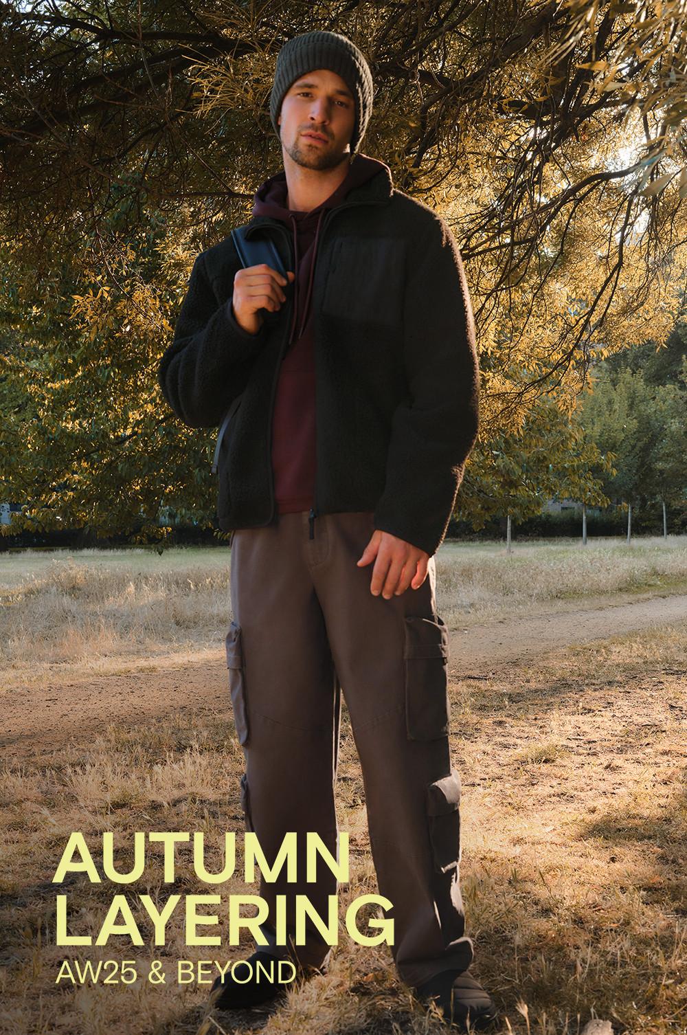 Person wearing black fleece jacket, burgundy hoodie, cargo trousers and beanie hat in autumn setting.