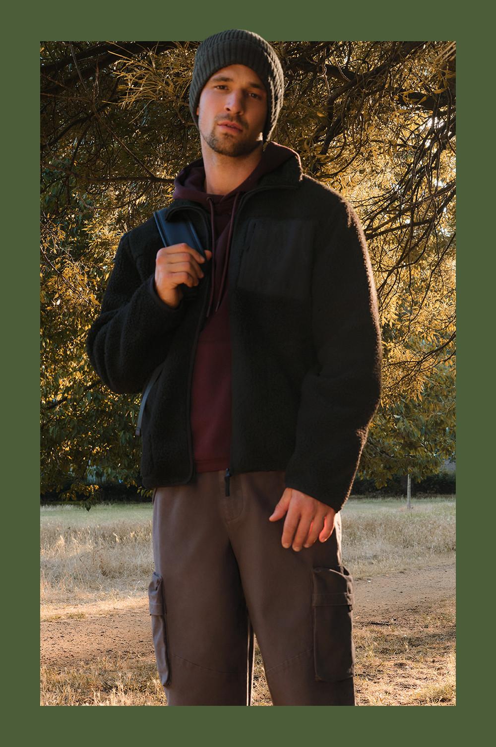 Person wearing black fleece jacket over burgundy hoodie with gray knit beanie and brown cargo pants outdoors.