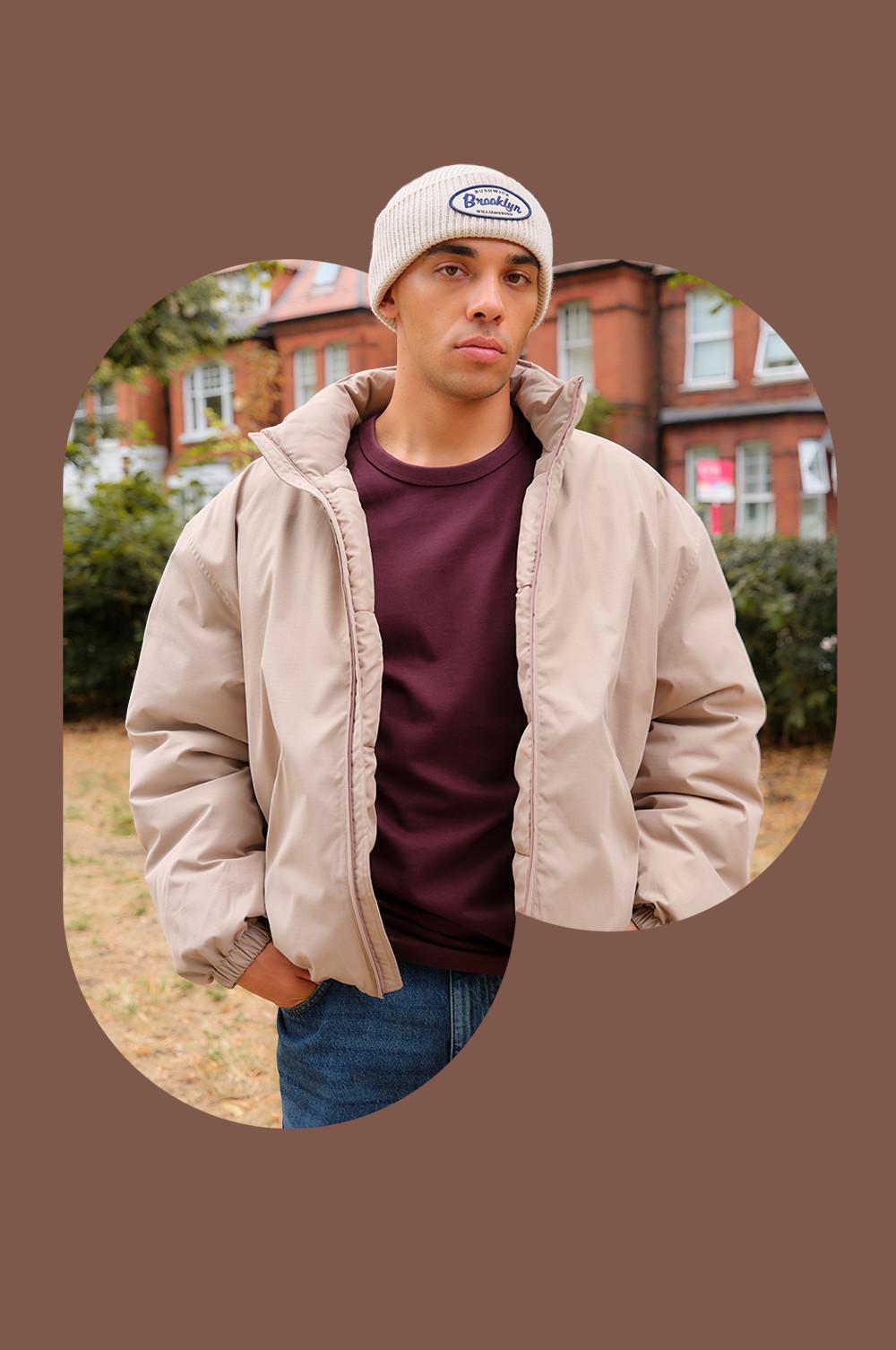 Person wearing cream Brooklyn beanie, beige jacket and burgundy sweater with jeans in outdoor setting.