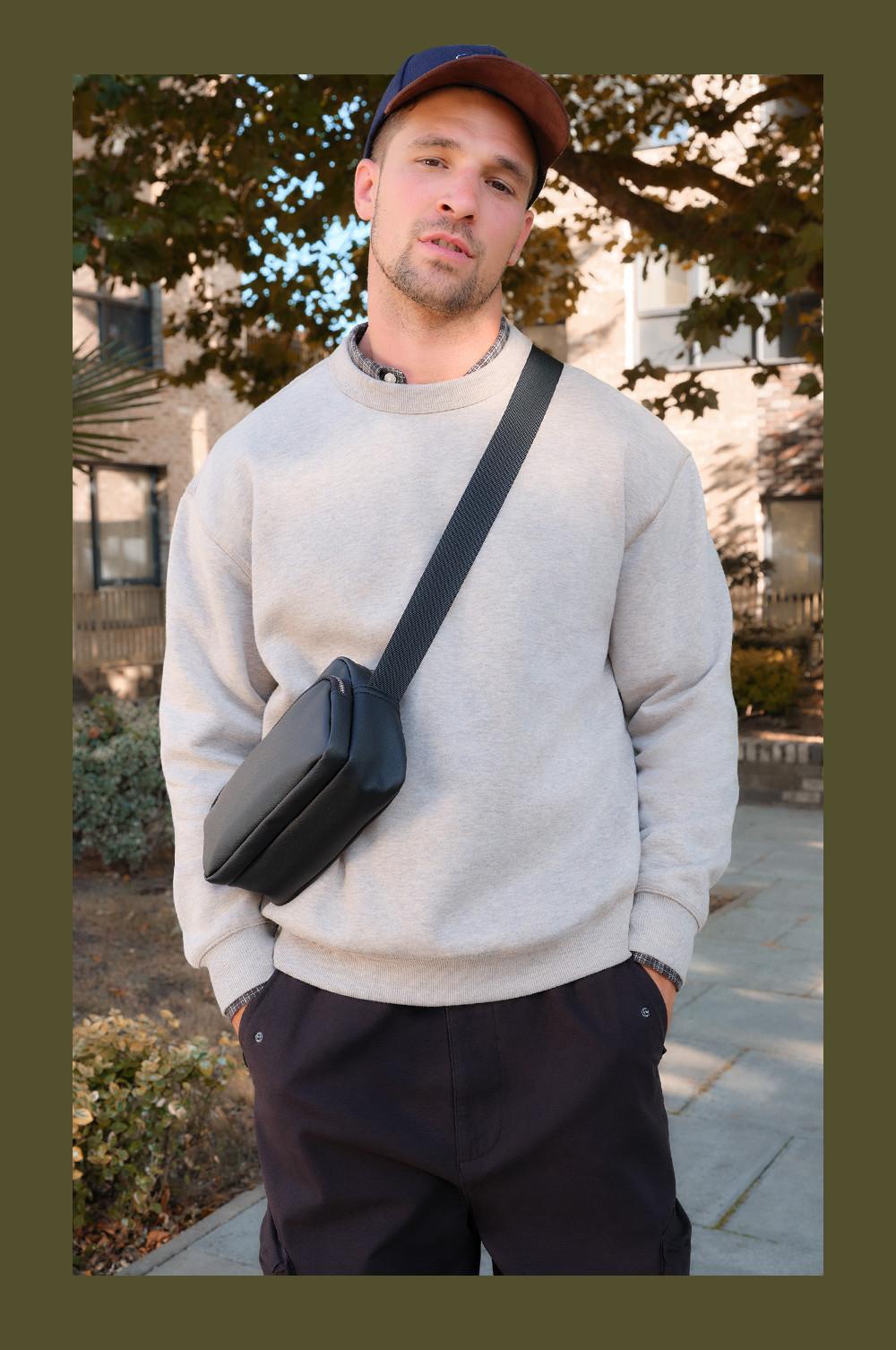 Person wearing cream sweatshirt with navy pants and baseball cap, carrying black crossbody bag outdoors.