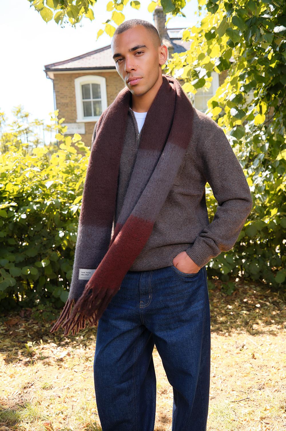 Gray sweater with burgundy scarf worn with denim jeans, photographed outdoors among fall foliage.