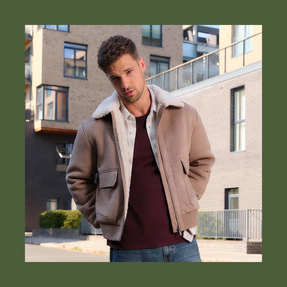 Beige shearling collar jacket worn over burgundy t-shirt and denim jeans, photographed in an urban setting.