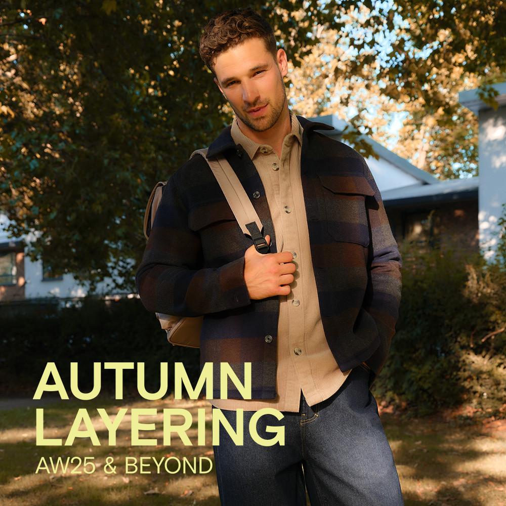 Person wearing striped navy overshirt with beige button-up underneath and shoulder bag in autumn setting.