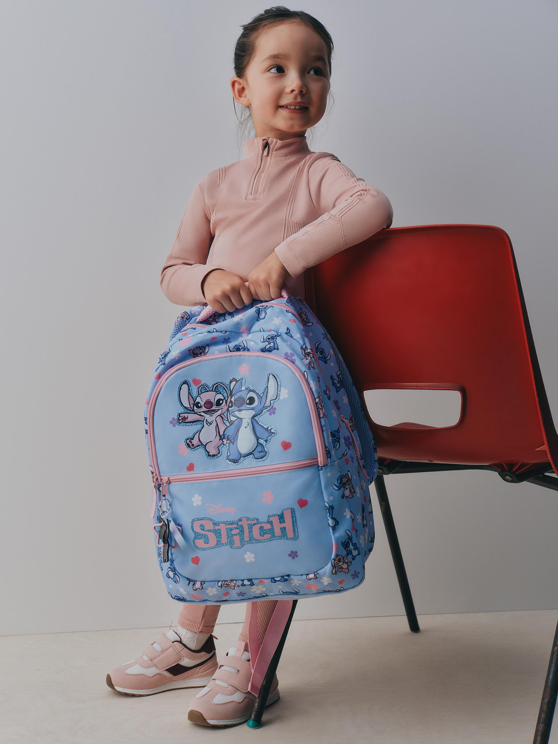 Model holding a blue rucksack wearing trainers and a pink loungewear set