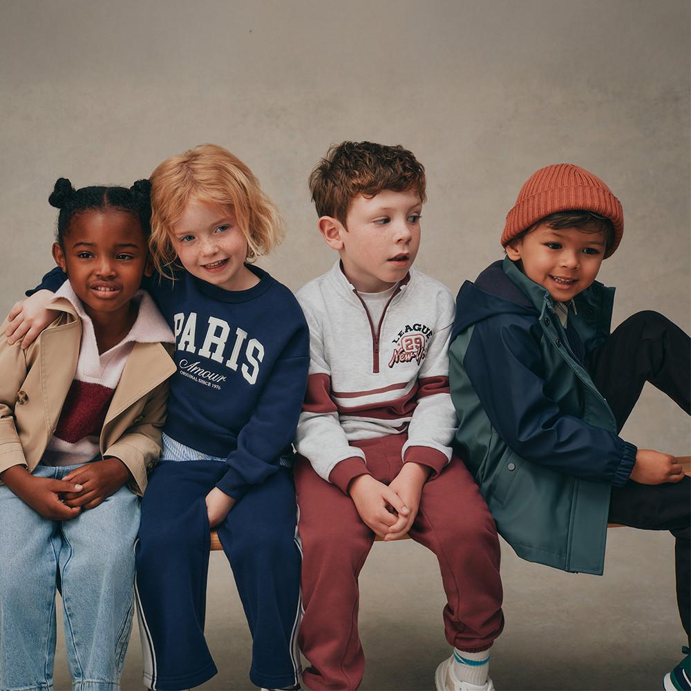 Enfants portant des tenues d'automne tendance, notamment un sweat-shirt Paris, un pull zippé et une veste de pluie et un bonnet orange.