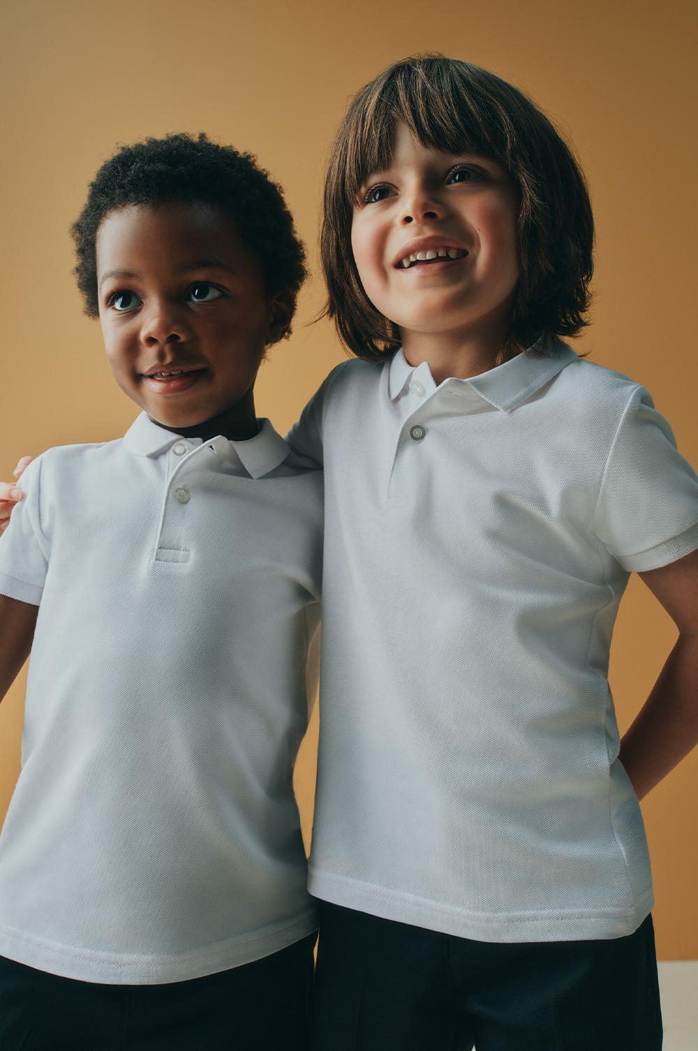 Two young children wearing white polo shirts standing side by side.