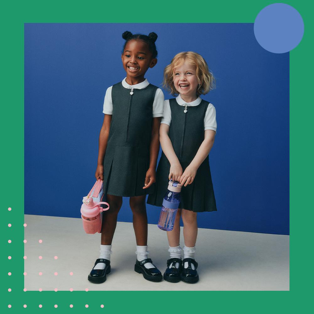 Two children wearing matching black school uniform dressed with white collared shirts and holding water bottles.
