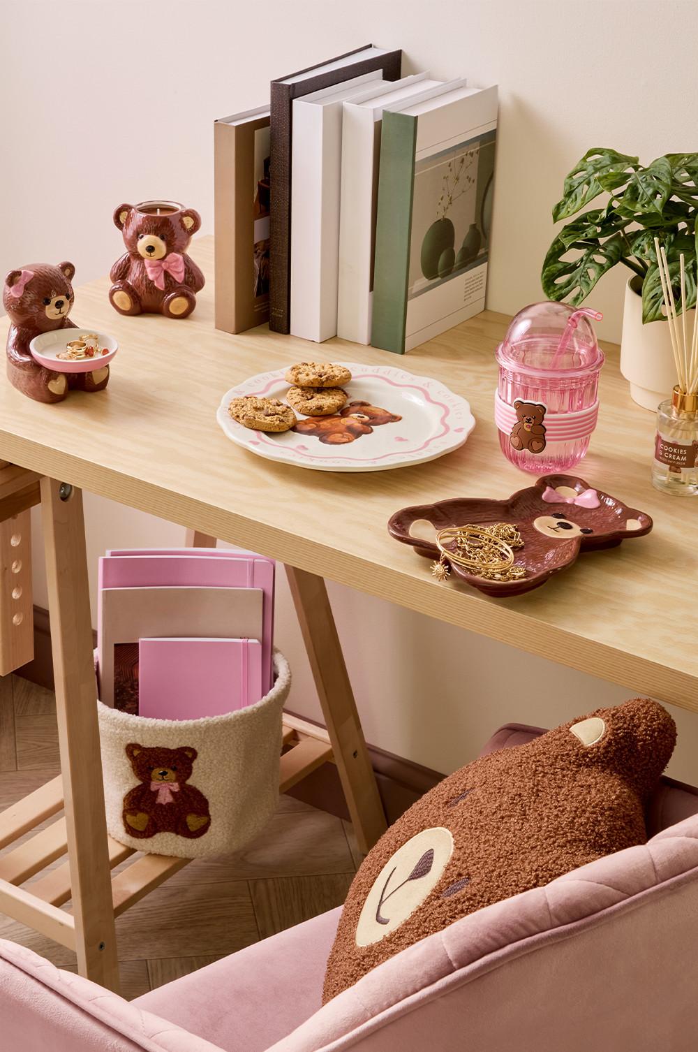 un bureau avec des accessoires sur le thème de l’ours, comme un coussin, un mug, une assiette, un gobelet avec paille et un panier
