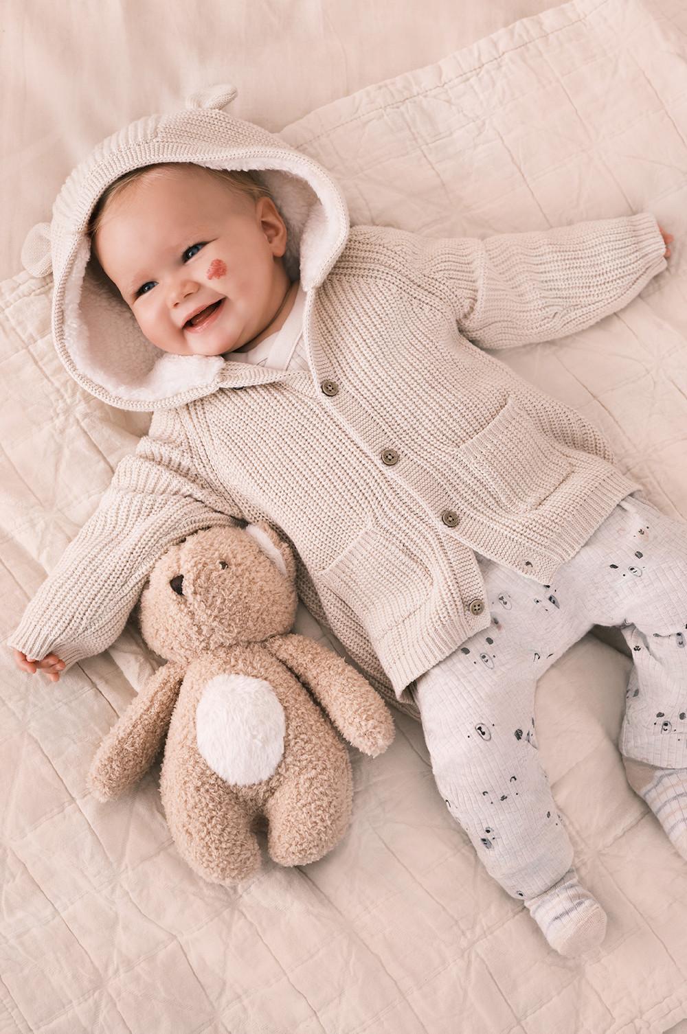 Il bebè indossa un cardigan crema lavorato a maglia con orecchie di orso