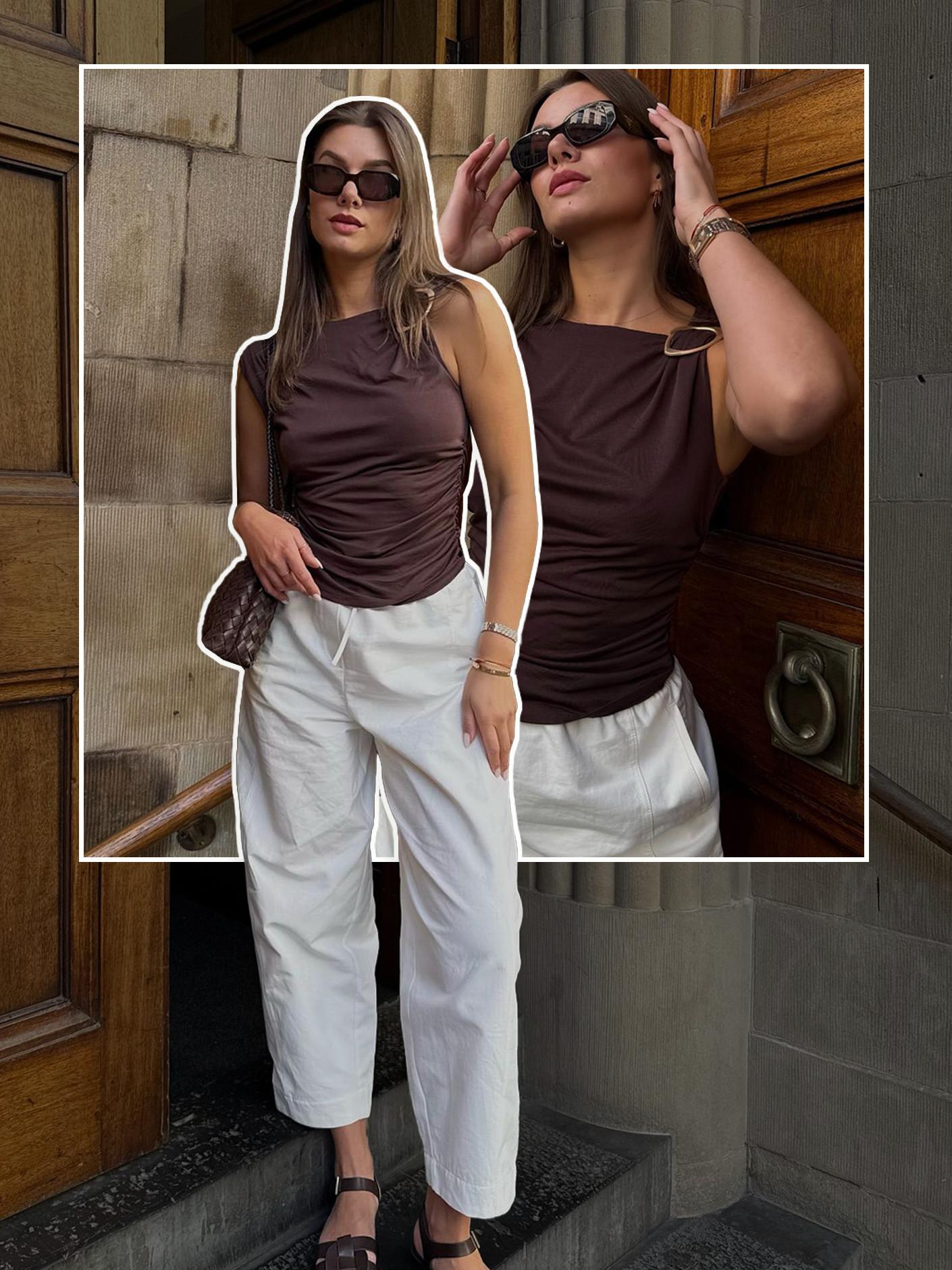 Model wearing brown sleeveless tops with white linen trousers and dark sunglasses, posing by a doorway.