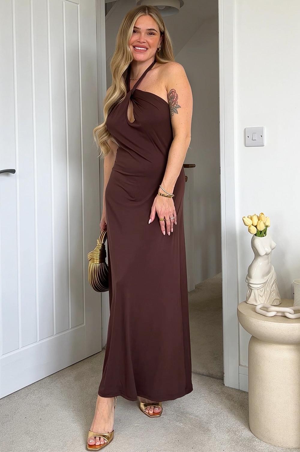 Brown halter neck maxi dress with keyhole detail, styled with gold-toned accessories and a striped handbag.