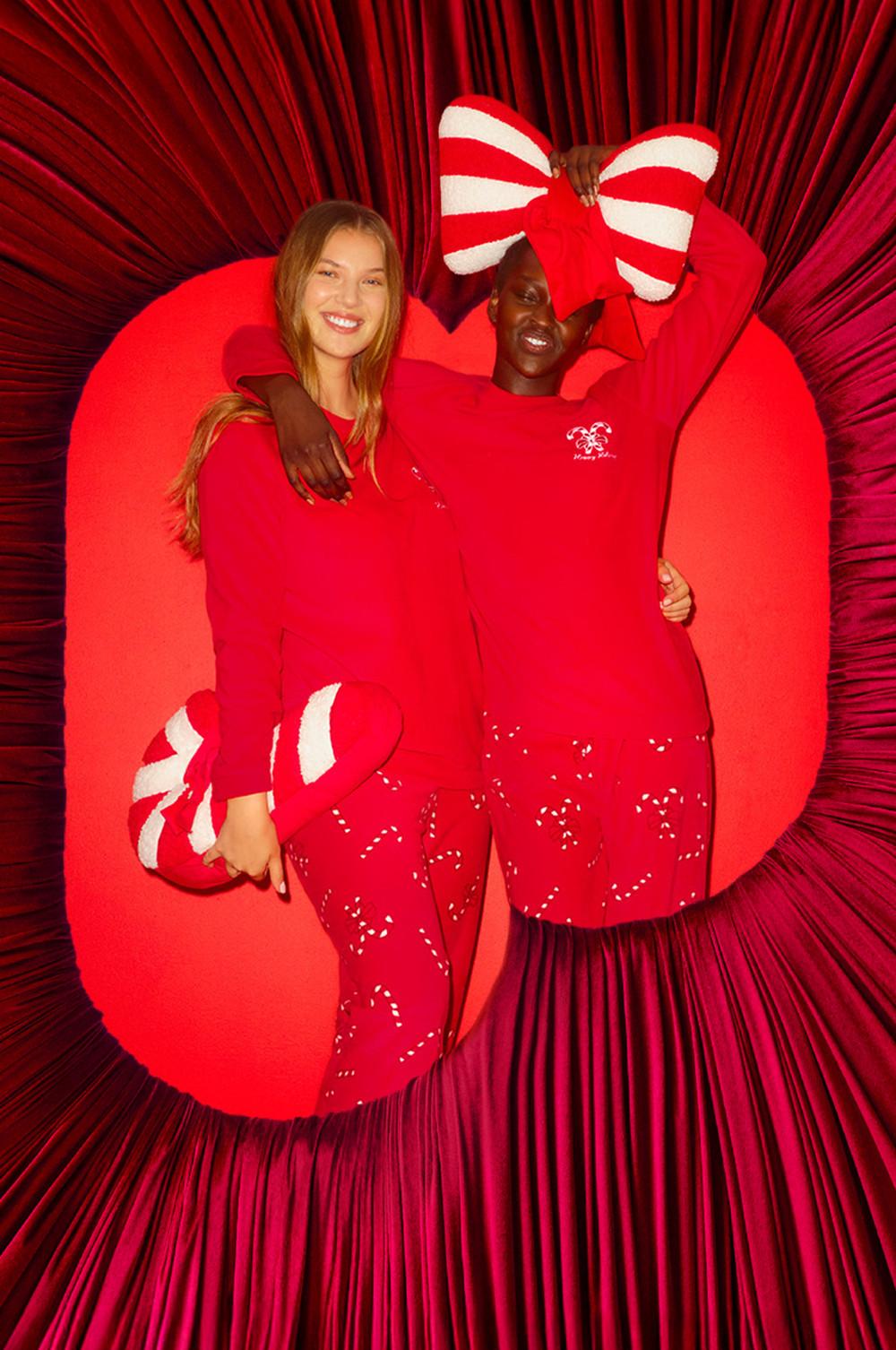 Due persone che indossano pigiami natalizi rossi coordinati con motivo a bastoncini di zucchero, con in mano accessori festivi a forma di fiocco.