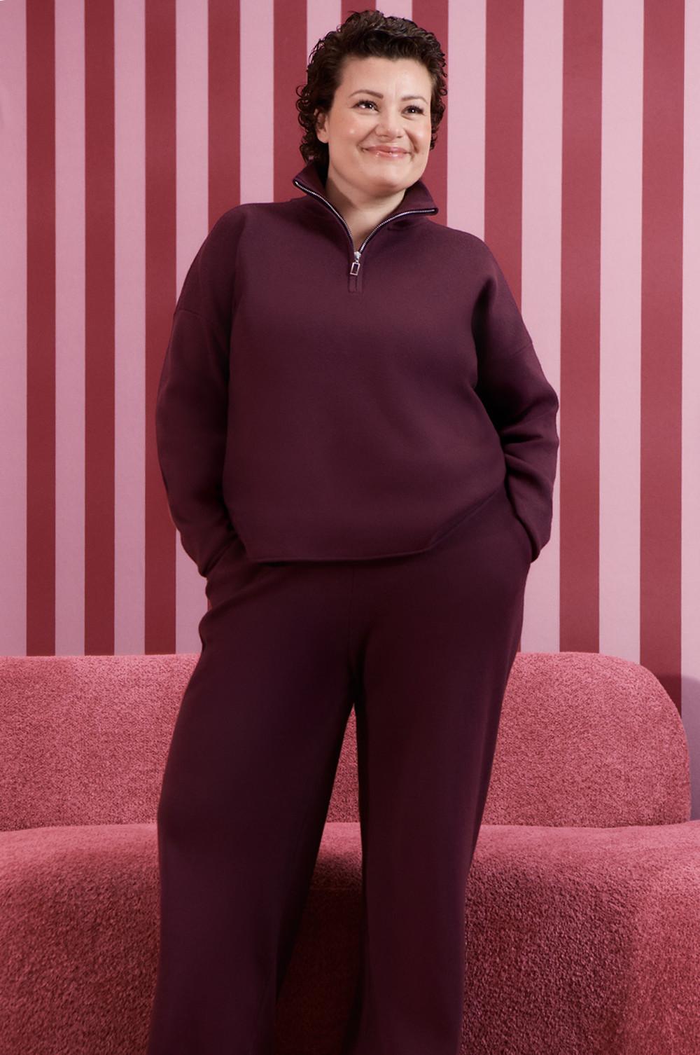 Persona che indossa un completo di abbigliamento da casa bordeaux con zip a un quarto su uno sfondo a righe rosa.