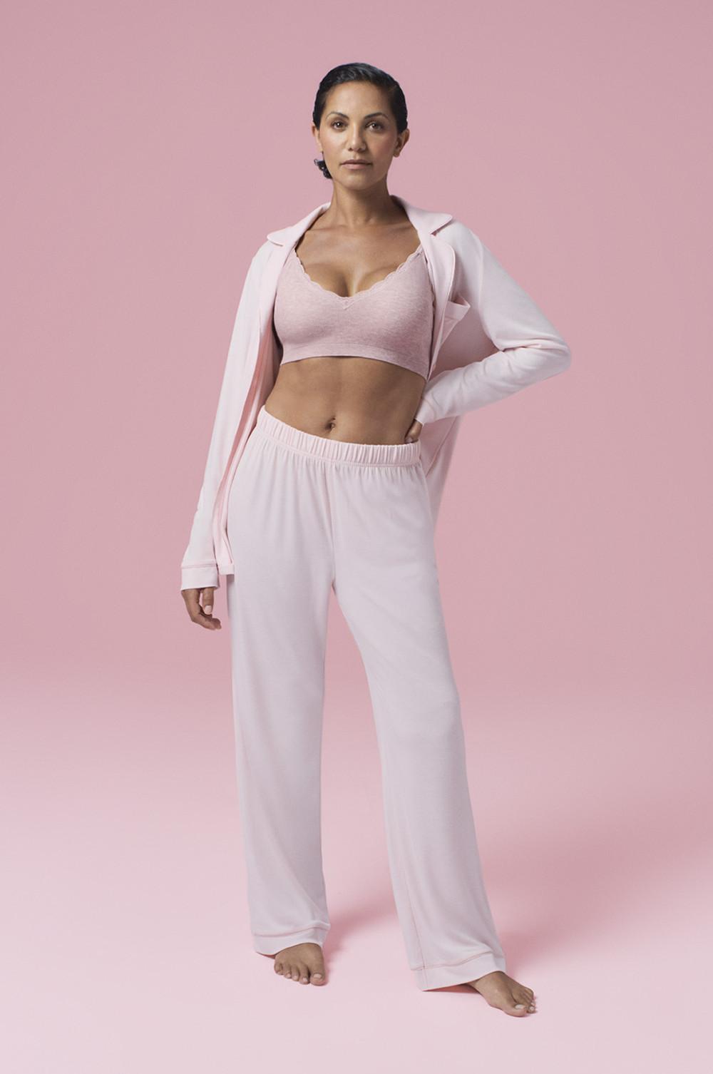 Persona che indossa un reggiseno sportivo rosa con un completo di abbigliamento da casa di giacca bianca e pantaloni abbinati su uno sfondo rosa.