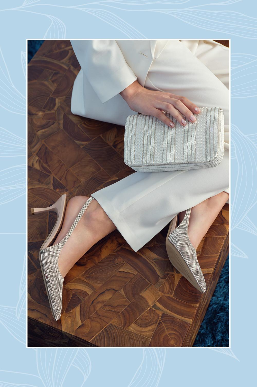 Model wearing white vest, blazer, pants, bow and rhinestone heels with clutch bag.