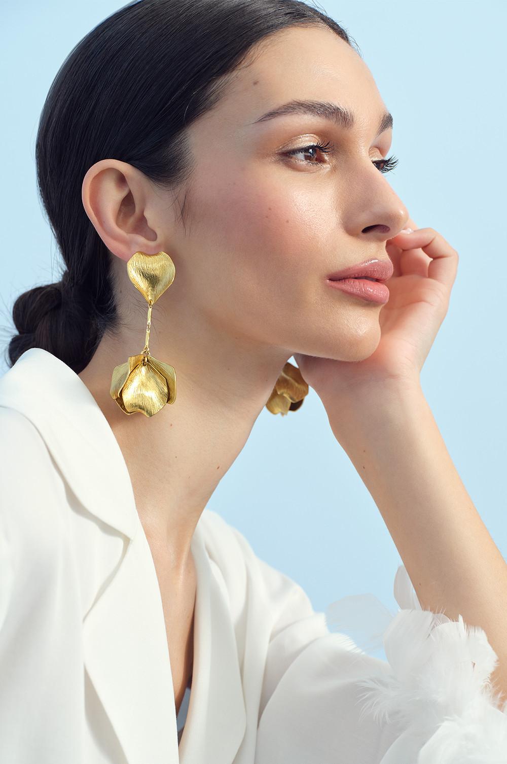 Model wearing gold earrings and white satin pyjama top with fluffy cuffs