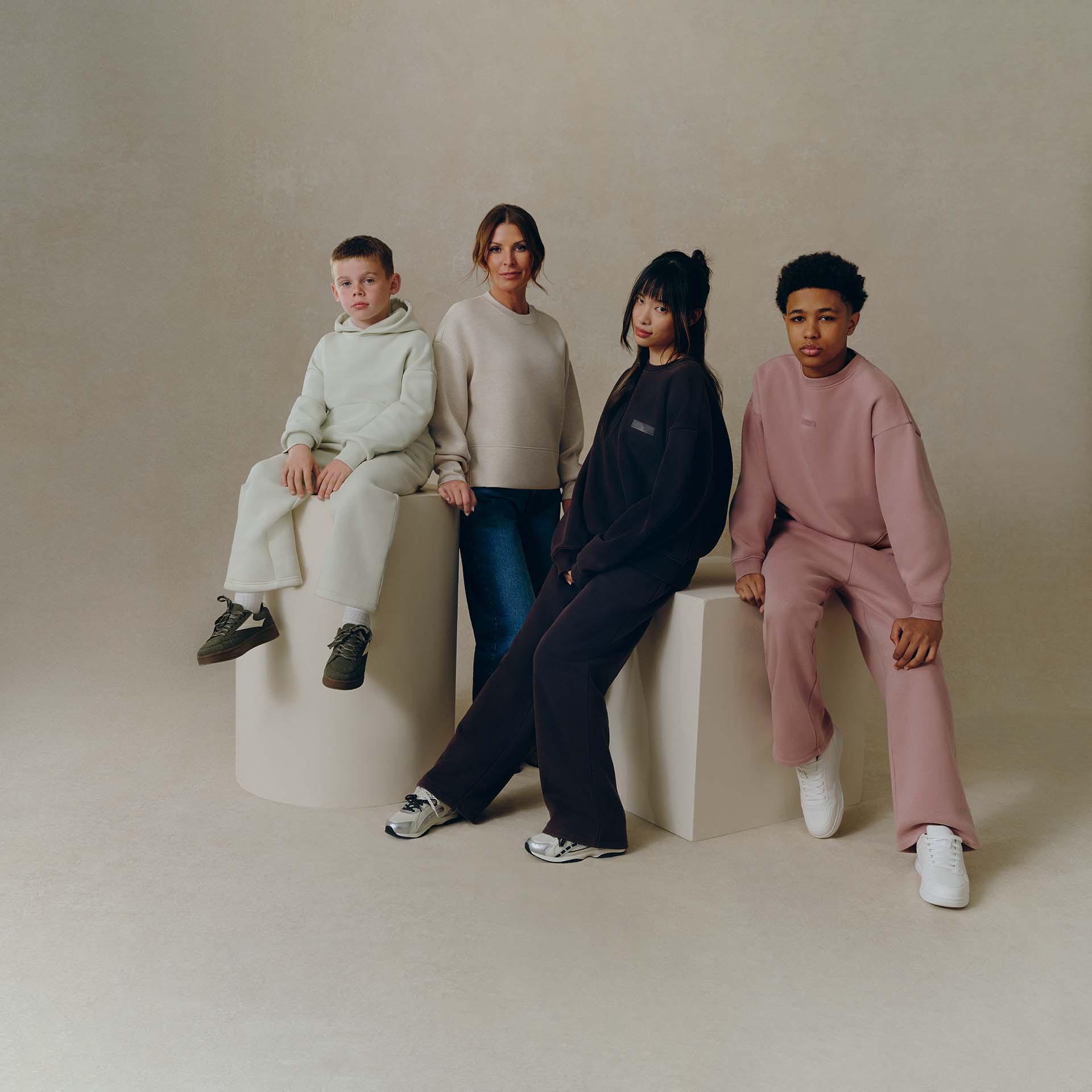 A woman and three children posing in casual loungewear, sitting on geometric blocks in a studio.