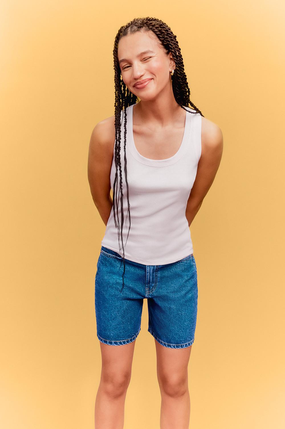 Model wearing white cami vest top and blue jorts