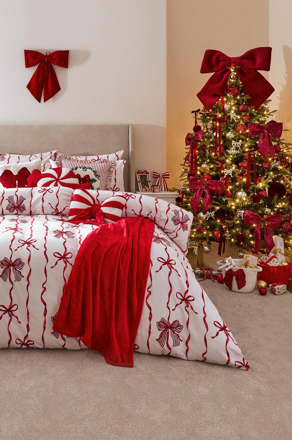Festive bedroom with red and white bow-patterned bedding, red throw blanket and decorated Christmas tree with presents.