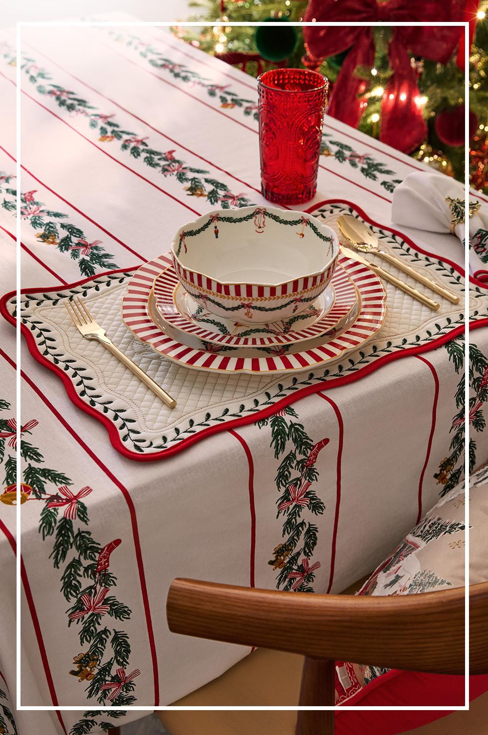Festive table setting with red-striped holiday dinnerware, gold cutlery, and red glass on Christmas-themed tablecloth.