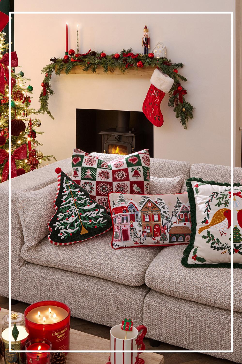 Cosy festive living room with decorated mantelpiece, Christmas stocking, and sofa adorned with seasonal cushions beside a lit fireplace.