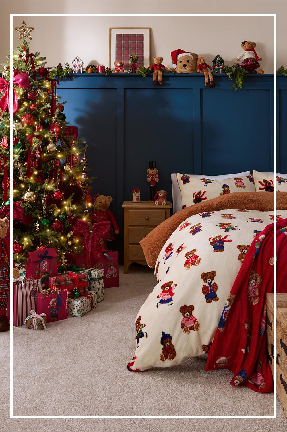 Festive bedroom with teddy bear patterned bedding, decorated Christmas tree, and blue panelled wall with holiday ornaments.
