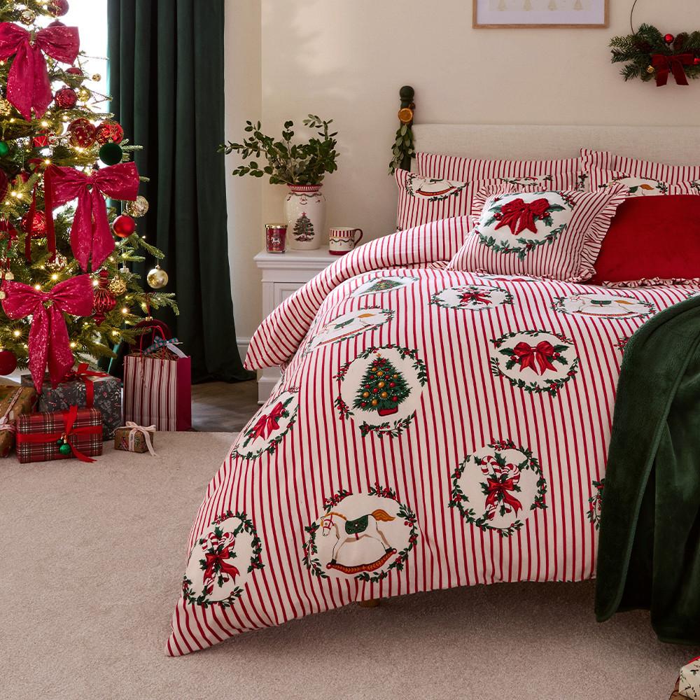 Festlich dekoriertes Schlafzimmer mit weiß-roter Bettwäsche mit Schleifenmuster, rotem Überwurf und geschmücktem Weihnachtsbaum mit Geschenken.