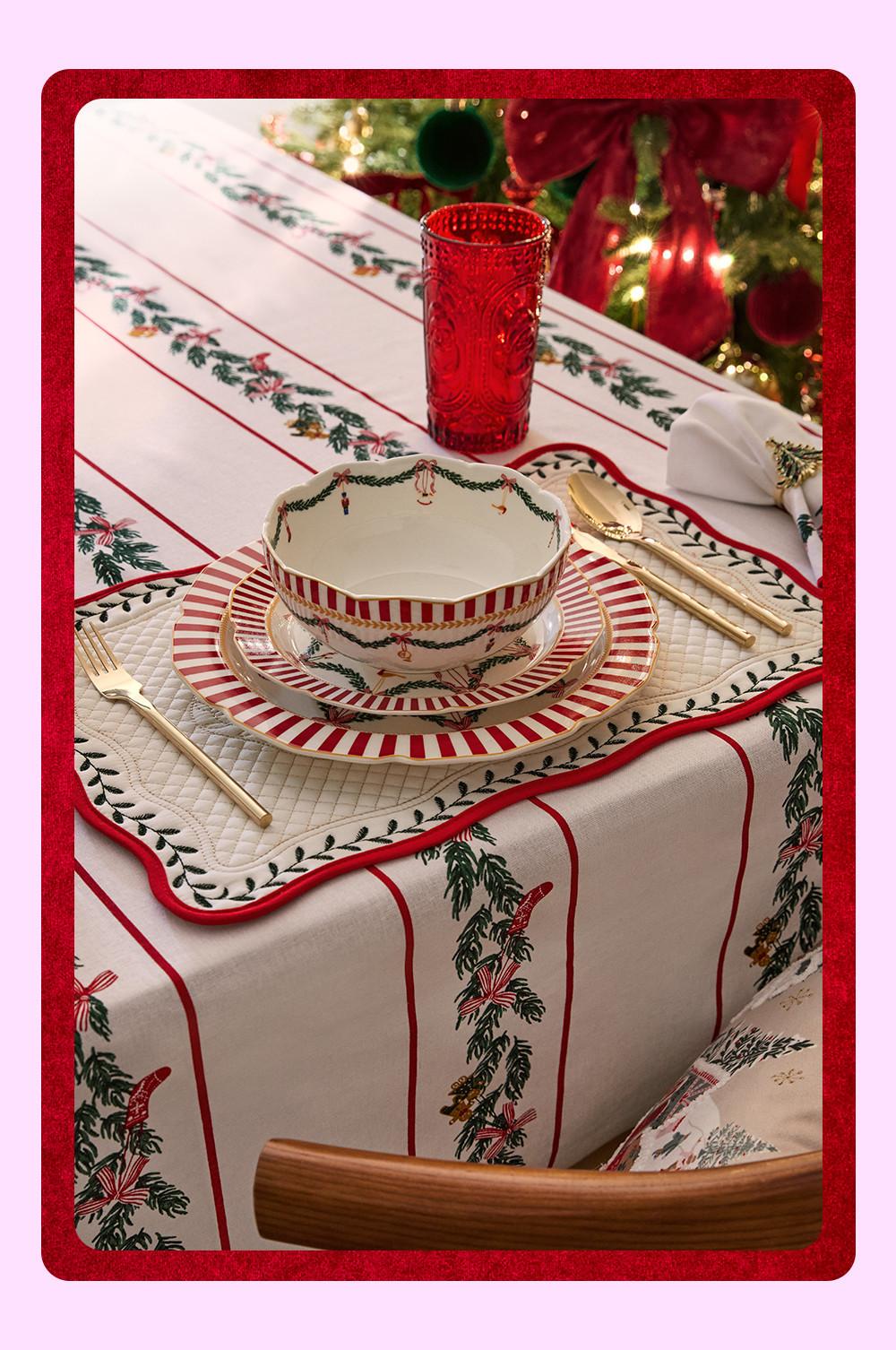 Decoración de mesa de temática navideña con vajilla de rayas rojas, cubiertos dorados y un vaso rojo, todo ello colocado sobre un mantel de temática navideña.