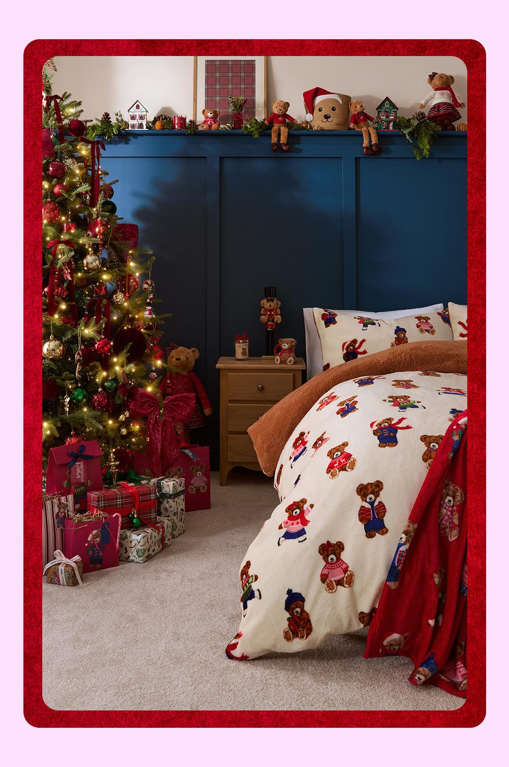 Dormitorio con ropa de cama con motivos de ositos, un árbol de Navidad adornado, una pared con paneles en azul y otros artículos navideños.