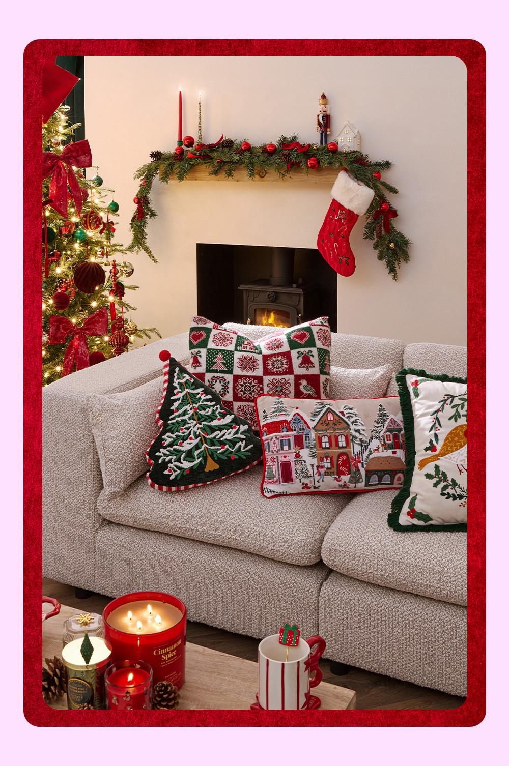 Acogedor salón con ambiente navideño y una chimenea encendida con un calcetín de Navidad colgando de la repisa y un sofá adornado con cojines con temática de la temporada.