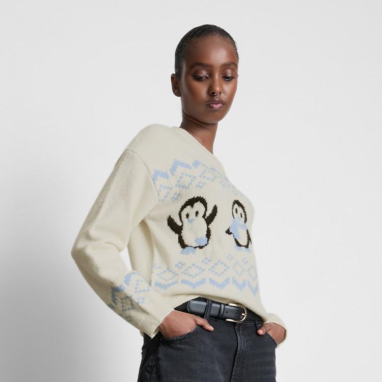 Cream jumper with penguin pattern and blue fair isle design, paired with dark denim jeans and black belt.
