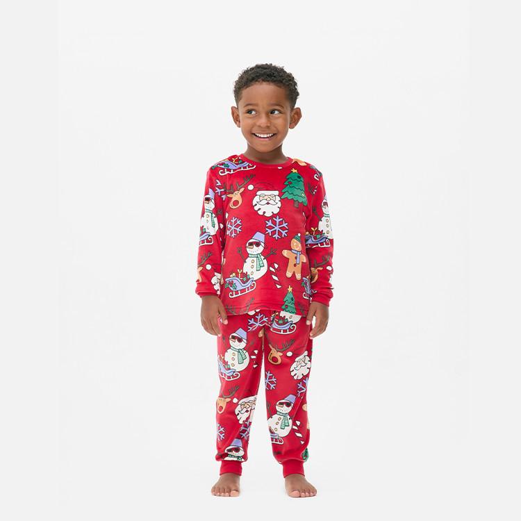 Child wearing red Christmas pyjamas featuring Santa, snowmen and festive characters.