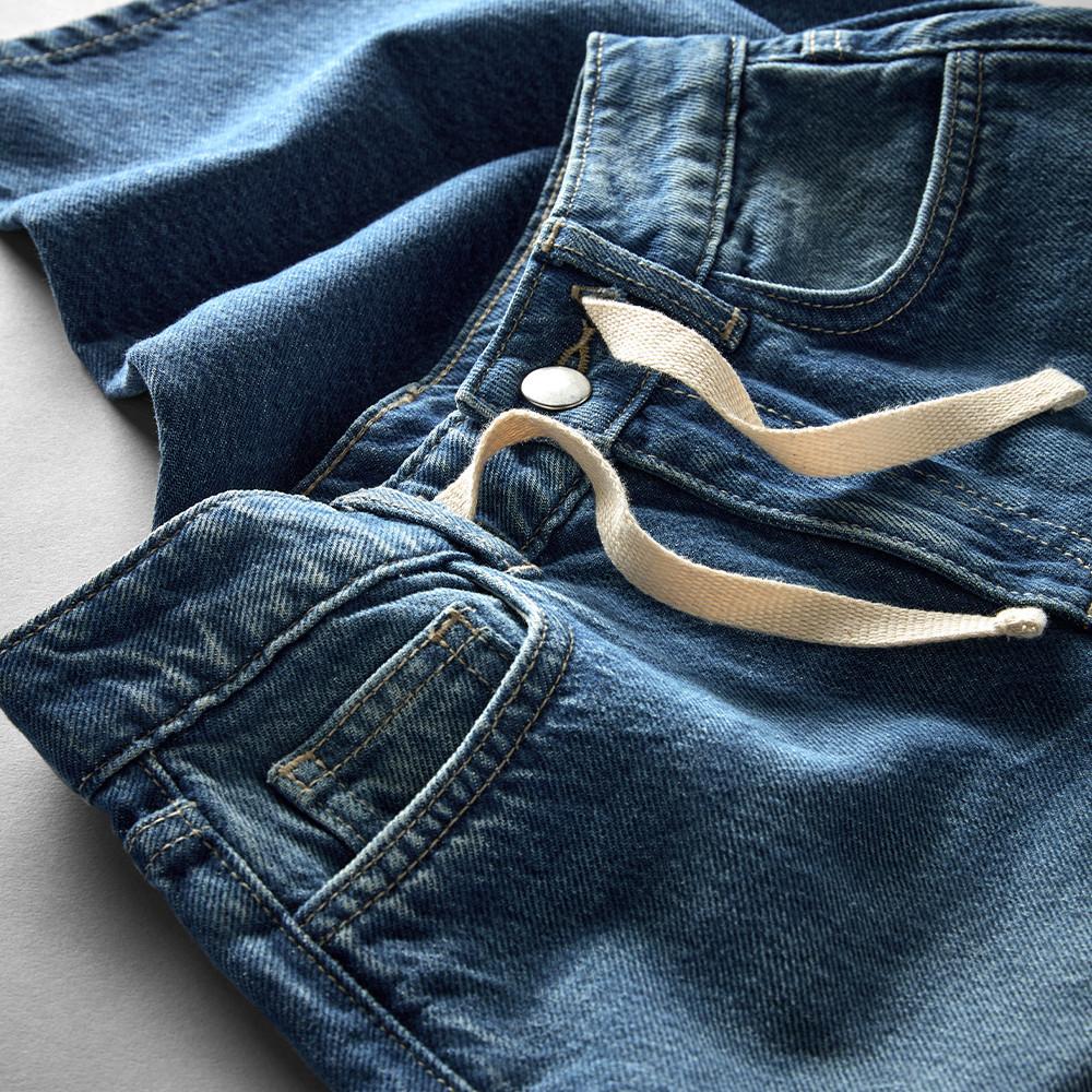 Close-up of blue denim jeans with cream drawstring waistband and metal button closure.
