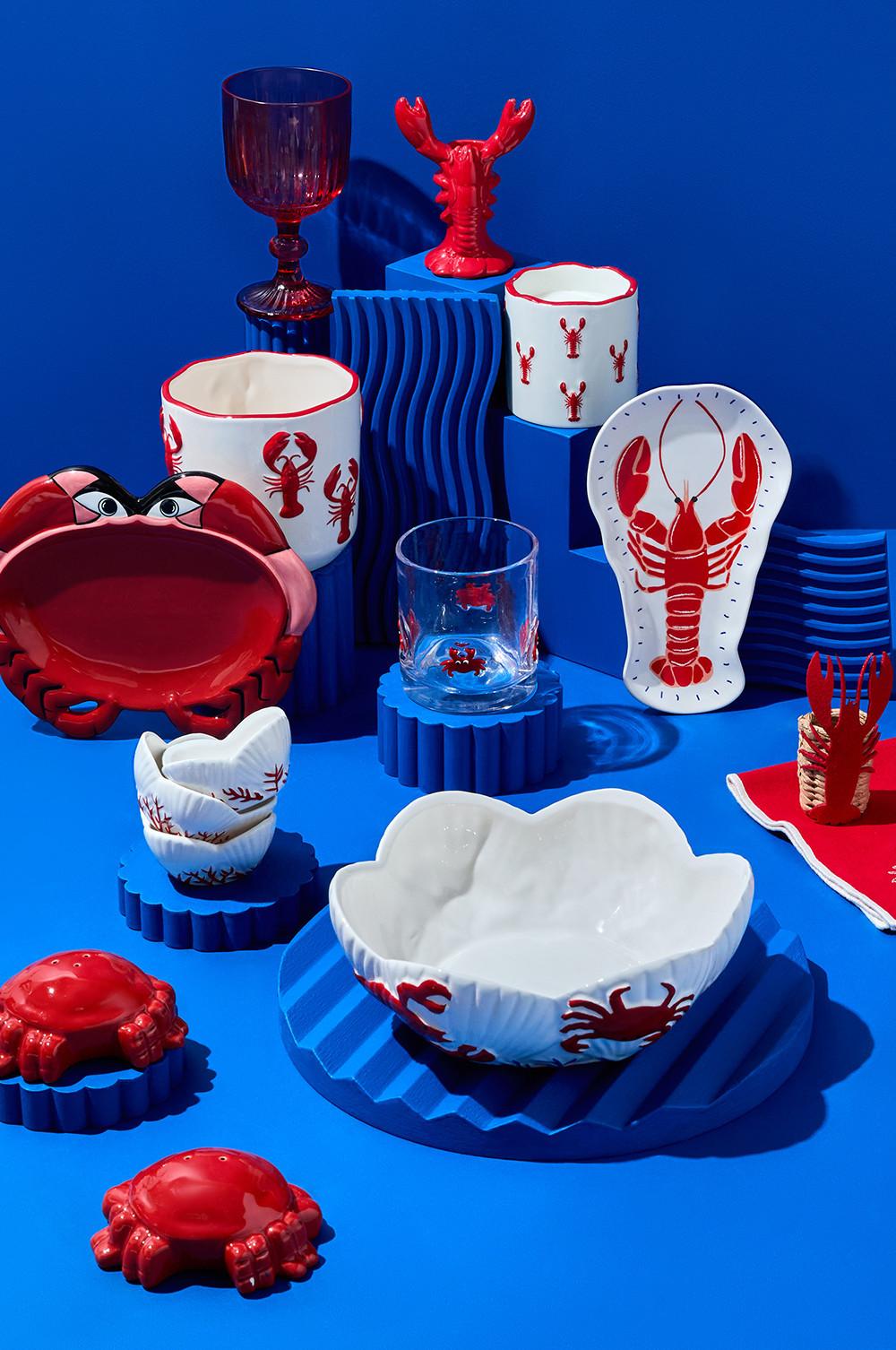 Servizio da tavola in ceramica con disegni di aragoste e granchi rossi disposti su una superficie blu.