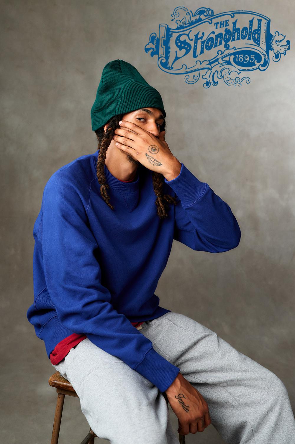 Model wears blue sweatshirt with green beanie