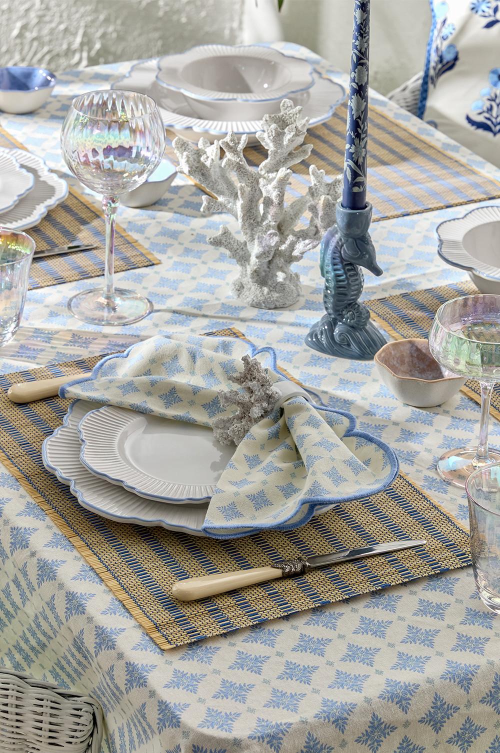Tisch im maritimen Stil mit blau gemustertem Geschirr, Serviettenringen im Korallen-Design und Seepferdchen-Kerzenständer auf gestreiften Platzdeckchen.