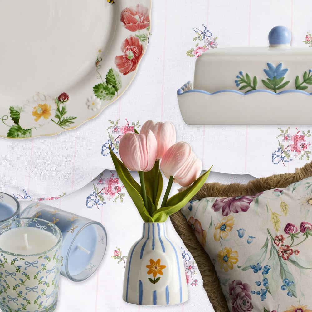 Pastel-coloured homeware collage with floral plates, yellow wine glass, and mint green vase with pink tulip against floral fabric.