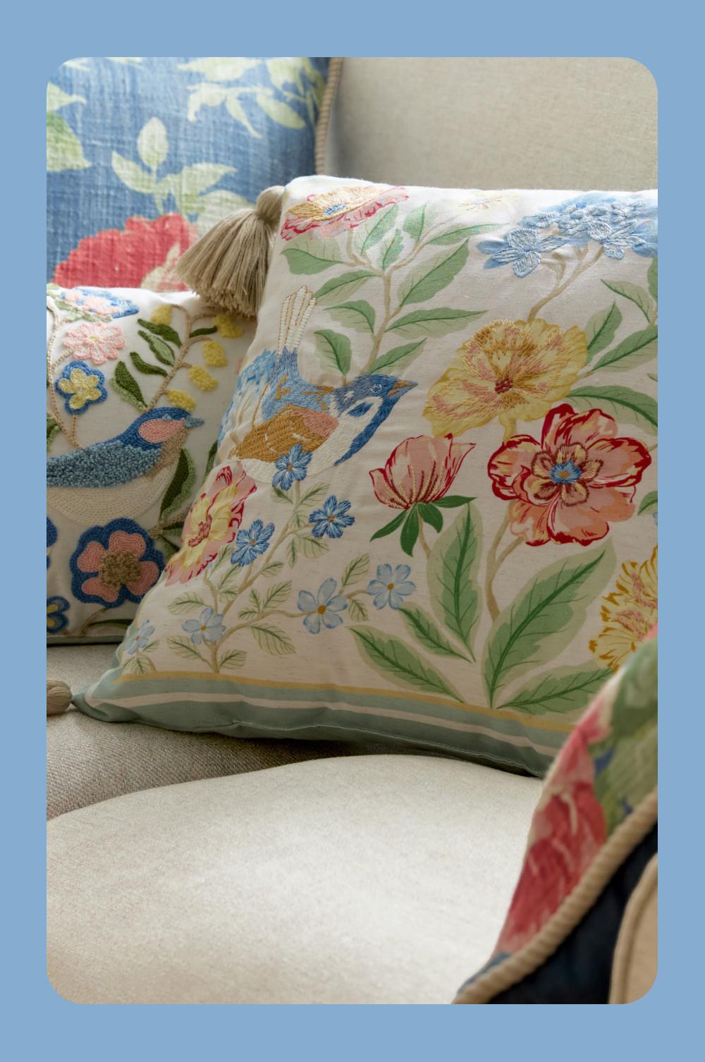 Decorative cushions with embroidered floral and bird designs arranged on a beige sofa.