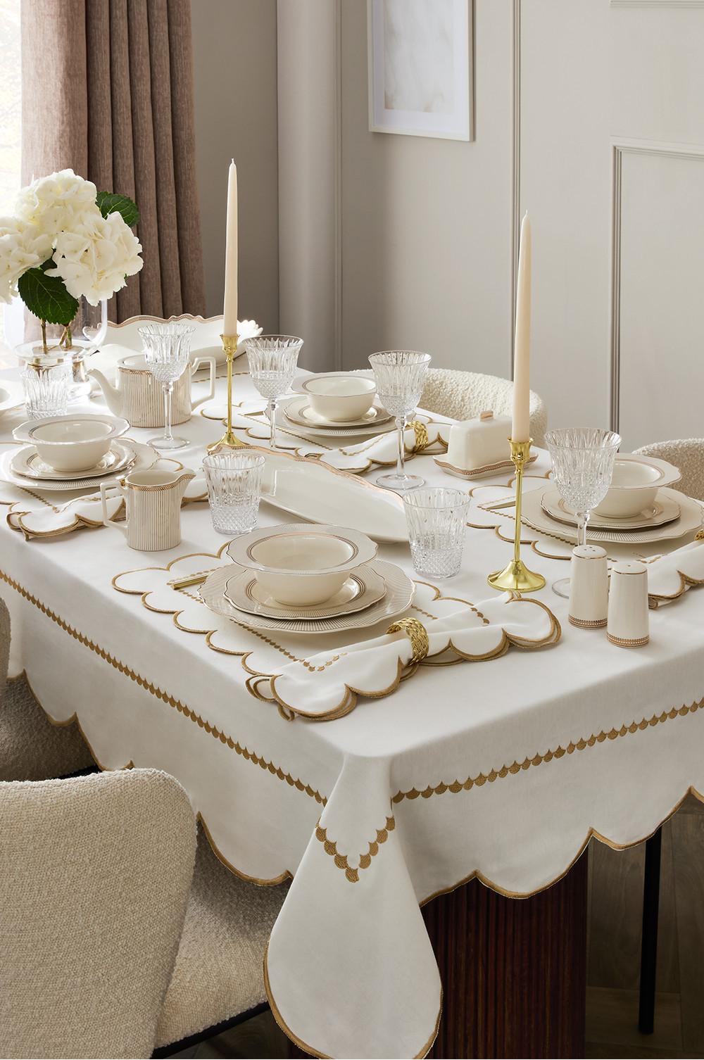 Elegant white and gold tablecloth with matching placemats, crystal glasses and cream dinnerware for a formal table setting.
