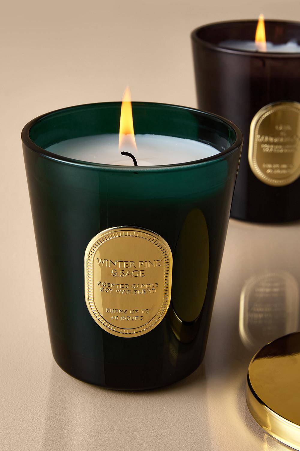 Lit Winter Pine & Sage scented candle in green glass container with gold label, alongside a black candle.