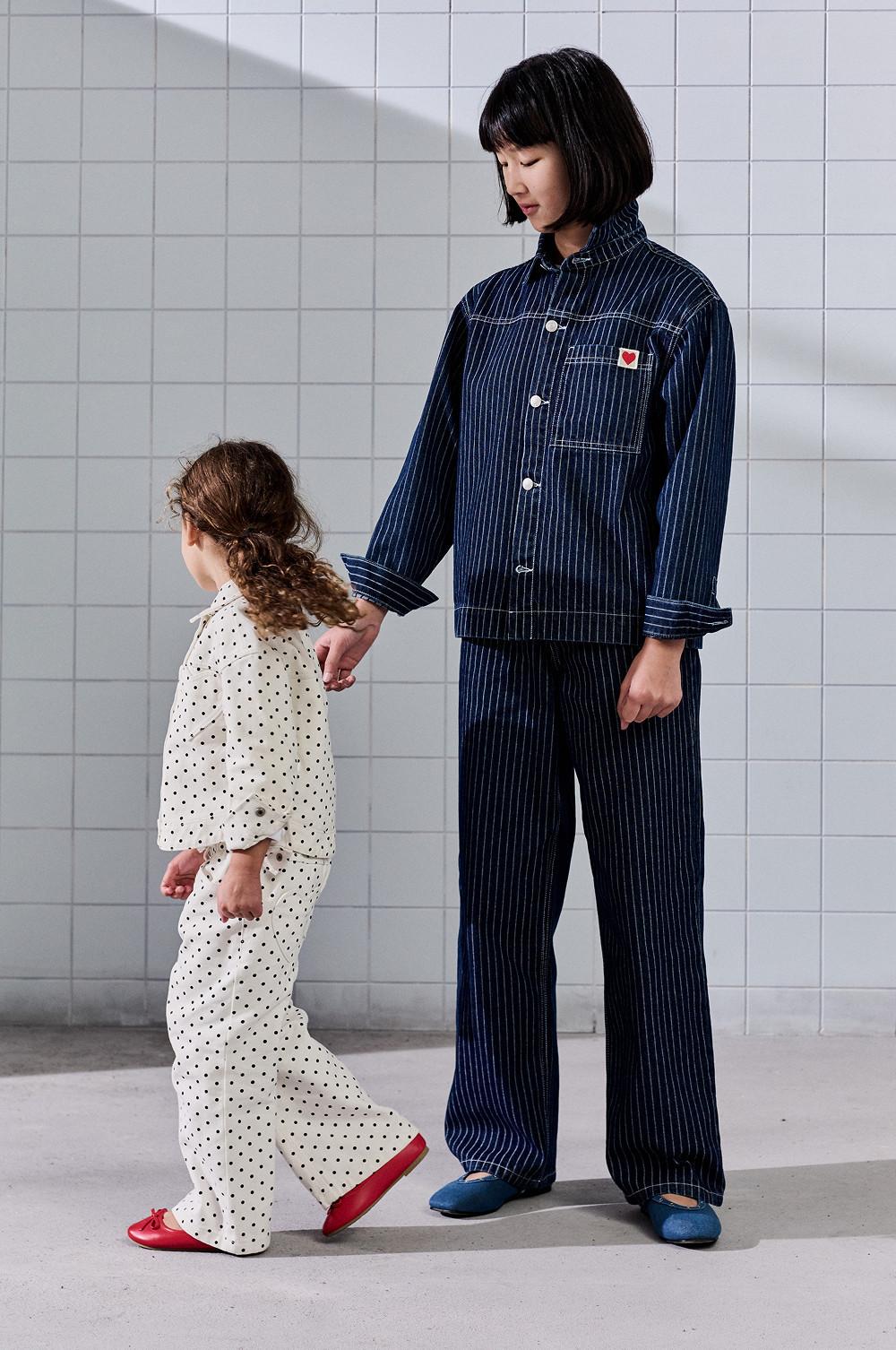 Pigiama a righe blu navy con dettaglio a forma di cuore accanto a un pigiama bianco a pois da bambina con pantofole rosse.