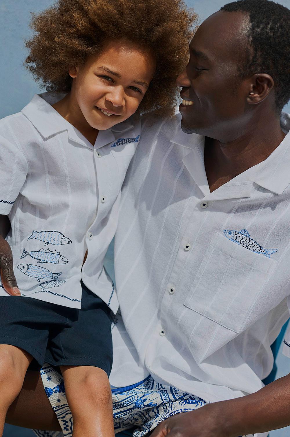 Adult and child smiling together, both wearing matching white shirts with blue fish embroidery.
