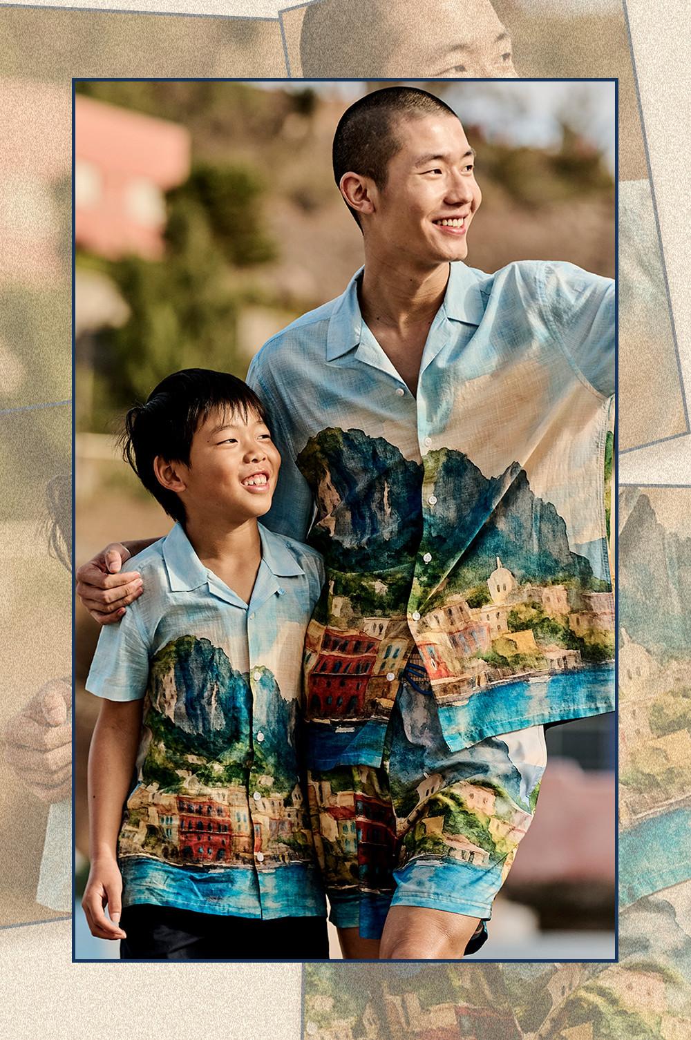Adult and child wearing matching light blue short-sleeved shirts with colourful coastal landscape print.