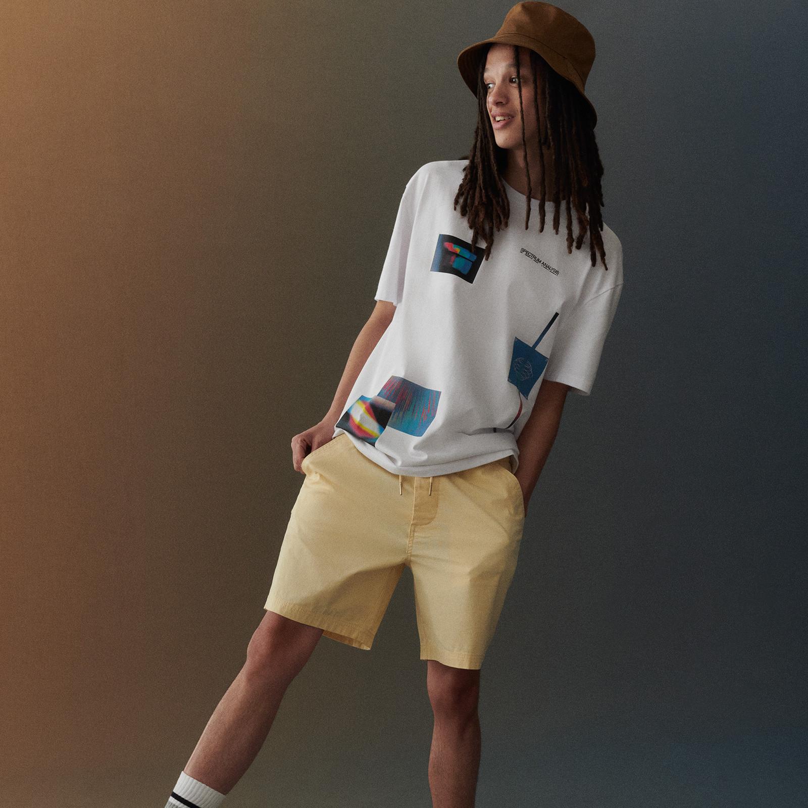 Model wears yellow shorts, white tshirt and bucket hat