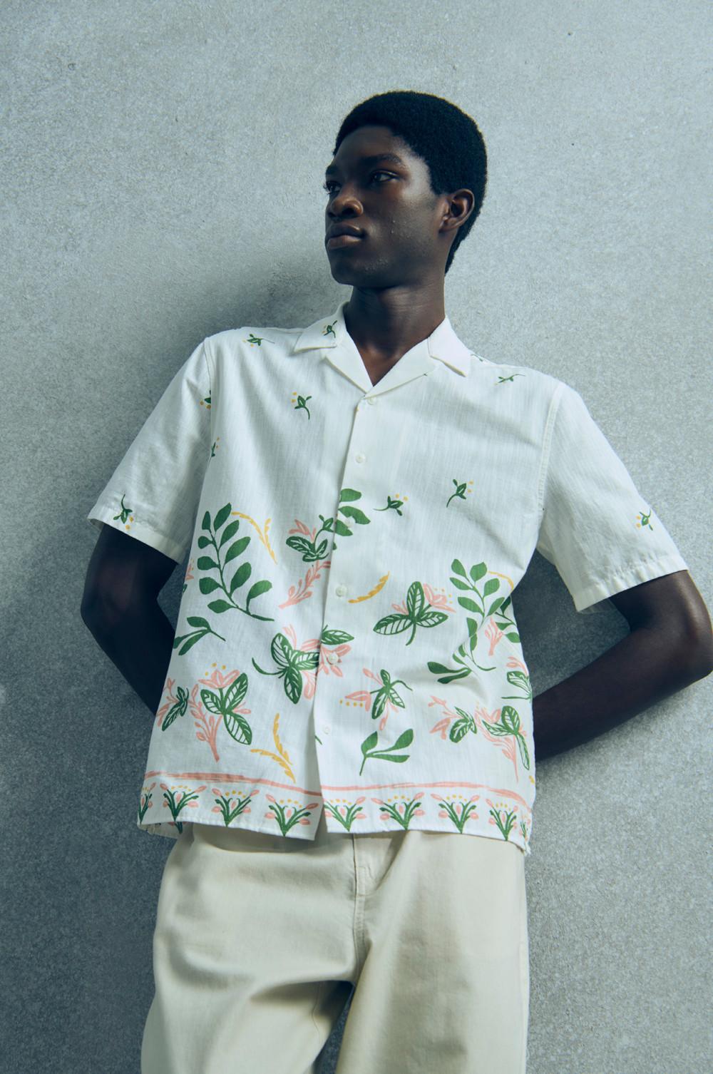 Weißes Kurzarmhemd mit botanischem Muster aus grünen Blättern und korallenroten Blumen zu cremefarbener Hose.