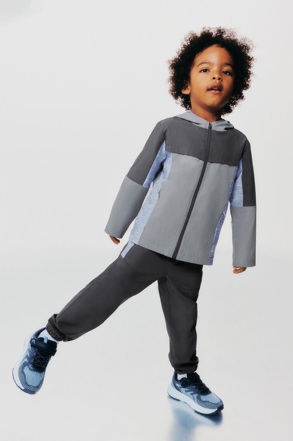 Child wearing gray and blue color-block zip-up jacket with matching sweatpants and athletic sneakers.